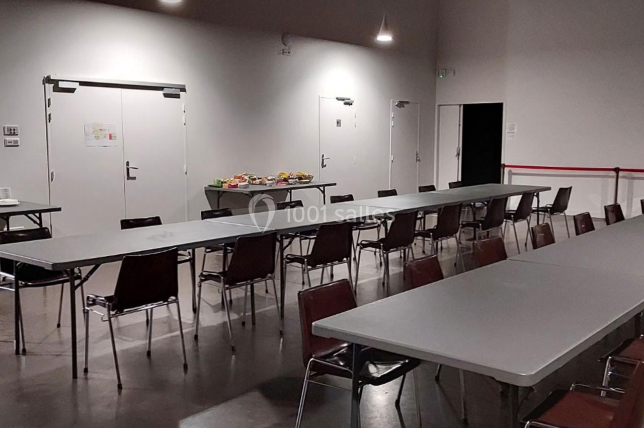 Salle avec des tables et chaises alignées, un buffet disposé au fond près des portes blanches.
