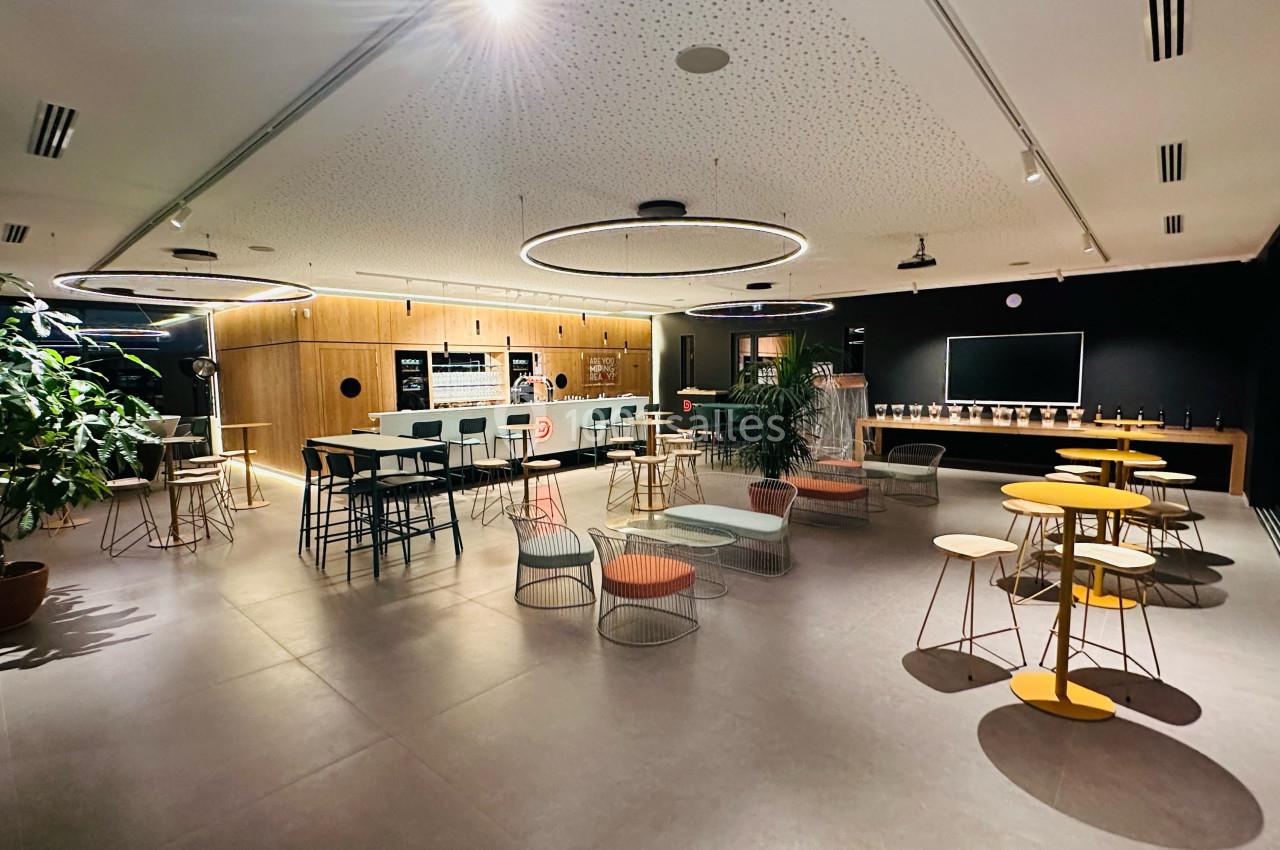 Salle moderne avec tables, chaises colorées, plantes et éclairage circulaire, aménagée pour des réunions ou des pauses.
