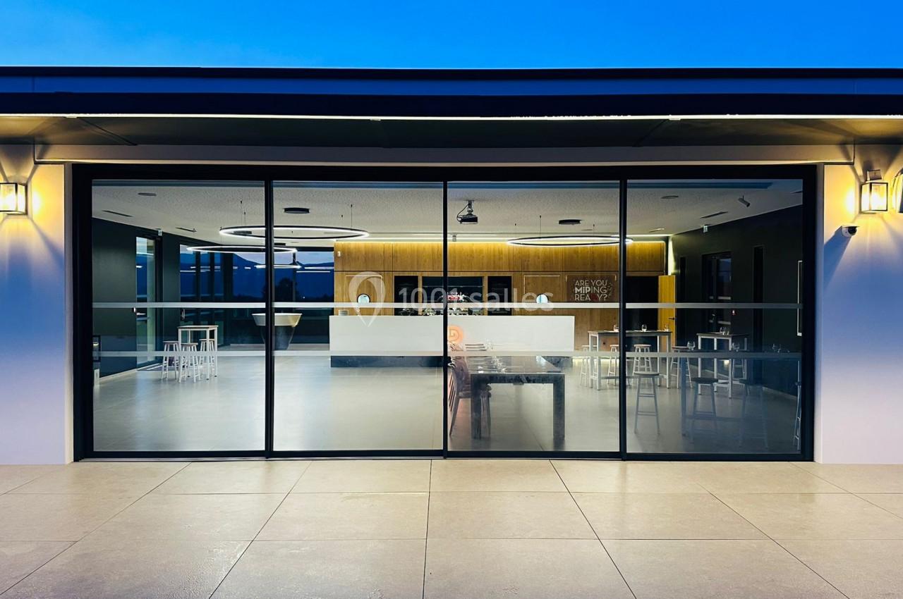 Façade vitrée d'un bâtiment moderne éclairé, laissant entrevoir un espace intérieur avec mobilier minimaliste.