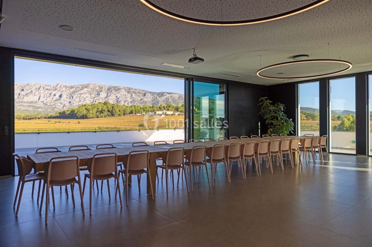 Salle de réunion lumineuse avec une grande table, vue sur un paysage de montagne et des baies vitrées ouvertes.