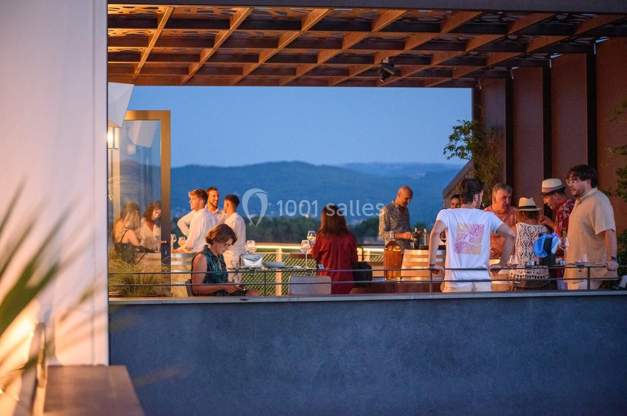 Groupe de personnes discutant et partageant un moment convivial sur une terrasse en soirée, avec vue sur des collines.