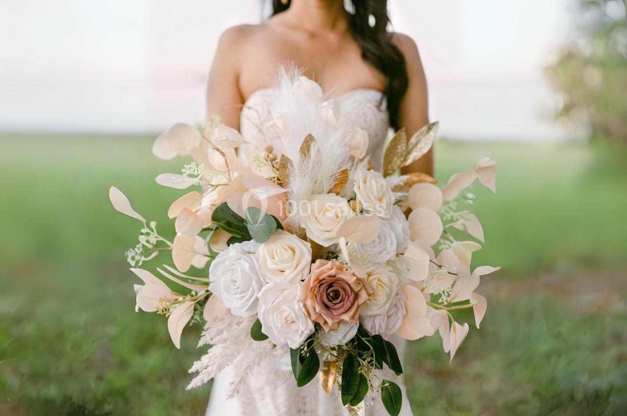 Femme en robe blanche tenant un bouquet de fleurs pastel avec des roses, des feuilles dorées et des plumes.