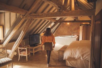 Femme de dos dans une chambre mansardée avec poutres apparentes, lit, télévision et baignoire en arrière-plan.