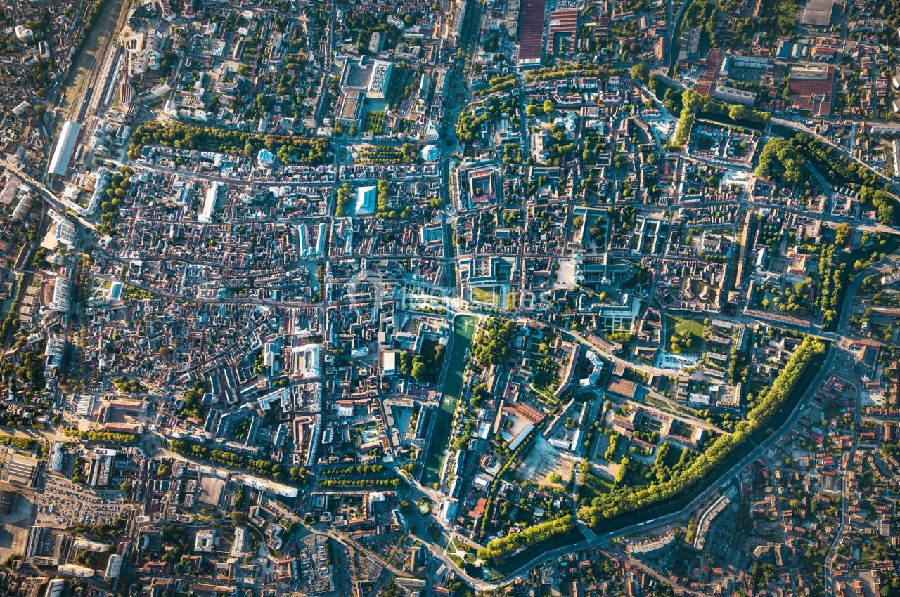 Vue aérienne d'une ville avec un centre historique dense, des rues sinueuses et des espaces verts entourant la zone urbaine.