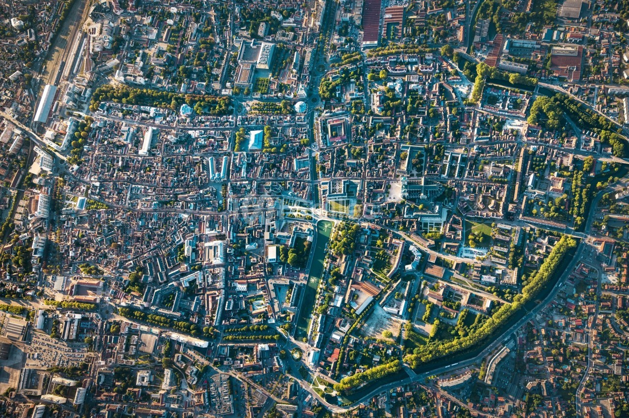 Vue aérienne d'une ville avec un centre historique dense, des rues sinueuses et des espaces verts entourant la zone urbaine.