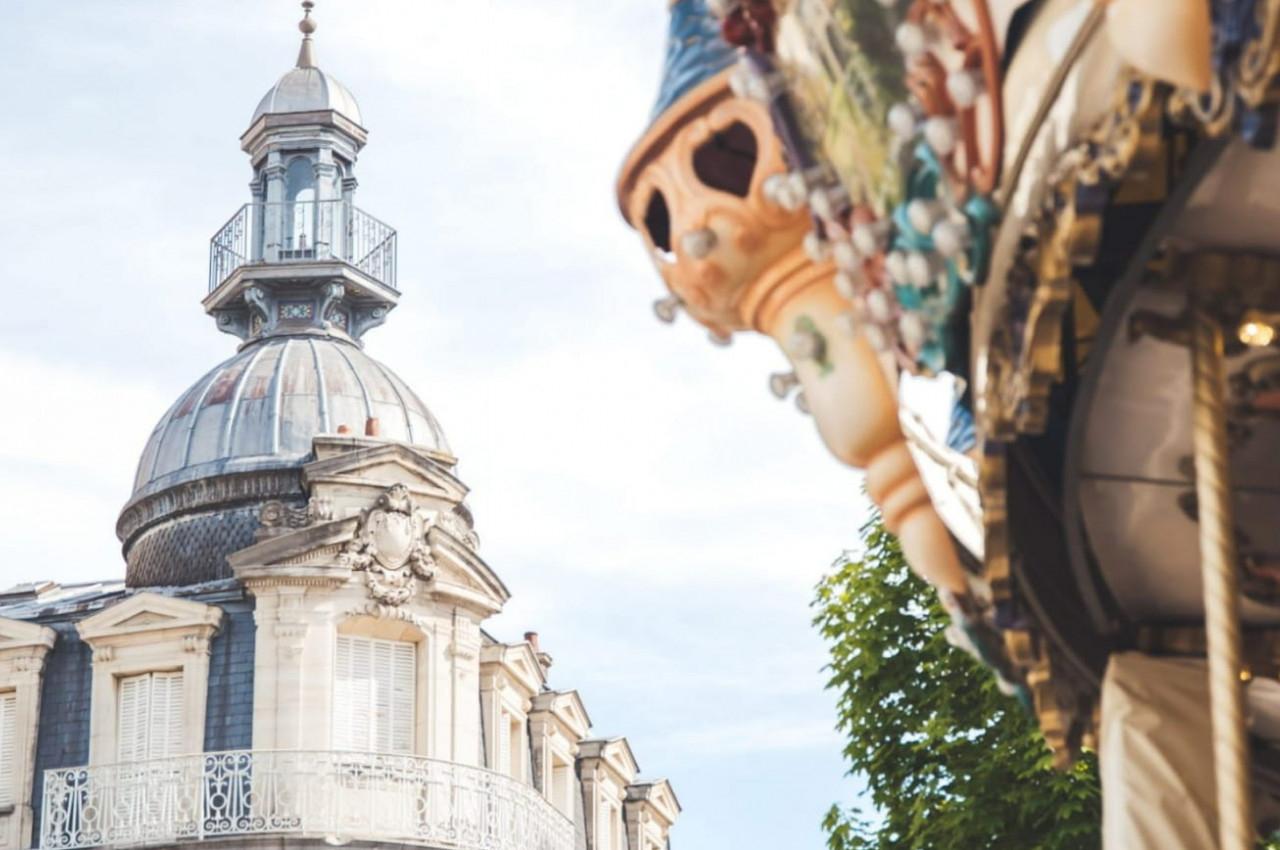 Dôme d'un bâtiment ancien avec balustrade, partiellement encadré par un carrousel décoré au premier plan.