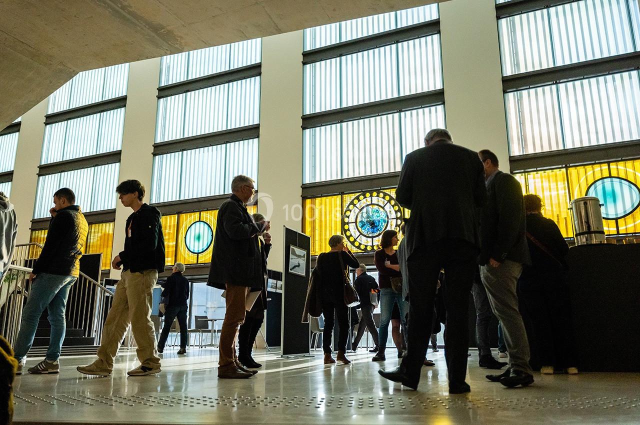 Groupe de personnes discutant dans un espace lumineux avec de grandes fenêtres et des vitraux colorés en arrière-plan.