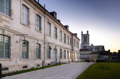 Femme de dos dans une chambre mansardée avec poutres apparentes, lit, télévision et baignoire en arrière-plan.