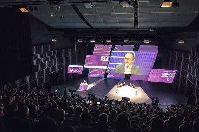 Femme de dos dans une chambre mansardée avec poutres apparentes, lit, télévision et baignoire en arrière-plan.