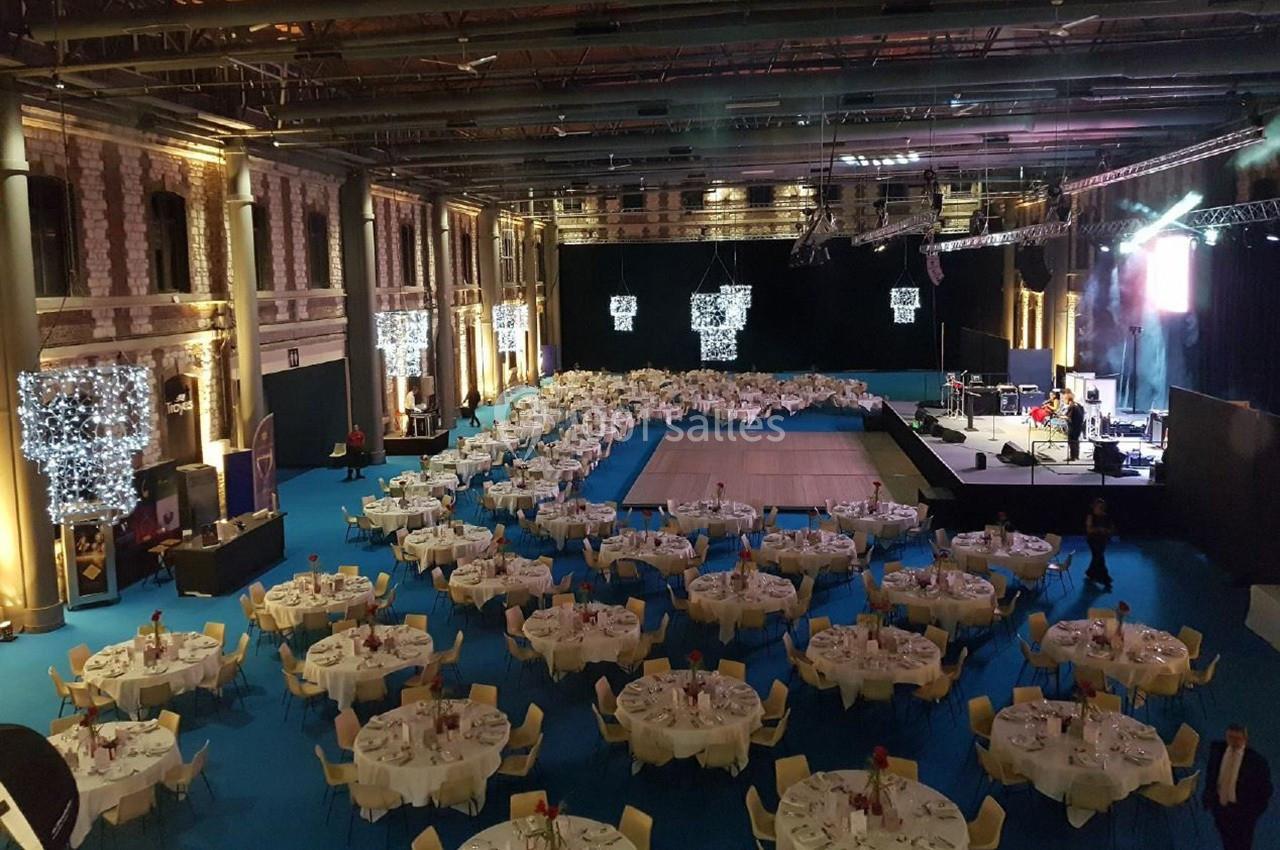 Salle de réception avec tables rondes dressées, piste de danse centrale et scène équipée pour un événement.