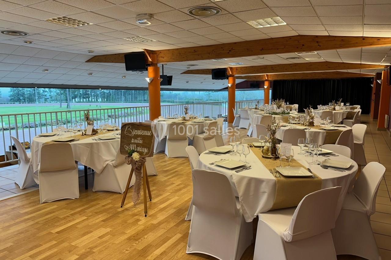 Salle de réception décorée avec des tables rondes dressées, nappes blanches et vue sur un espace extérieur verdoyant.