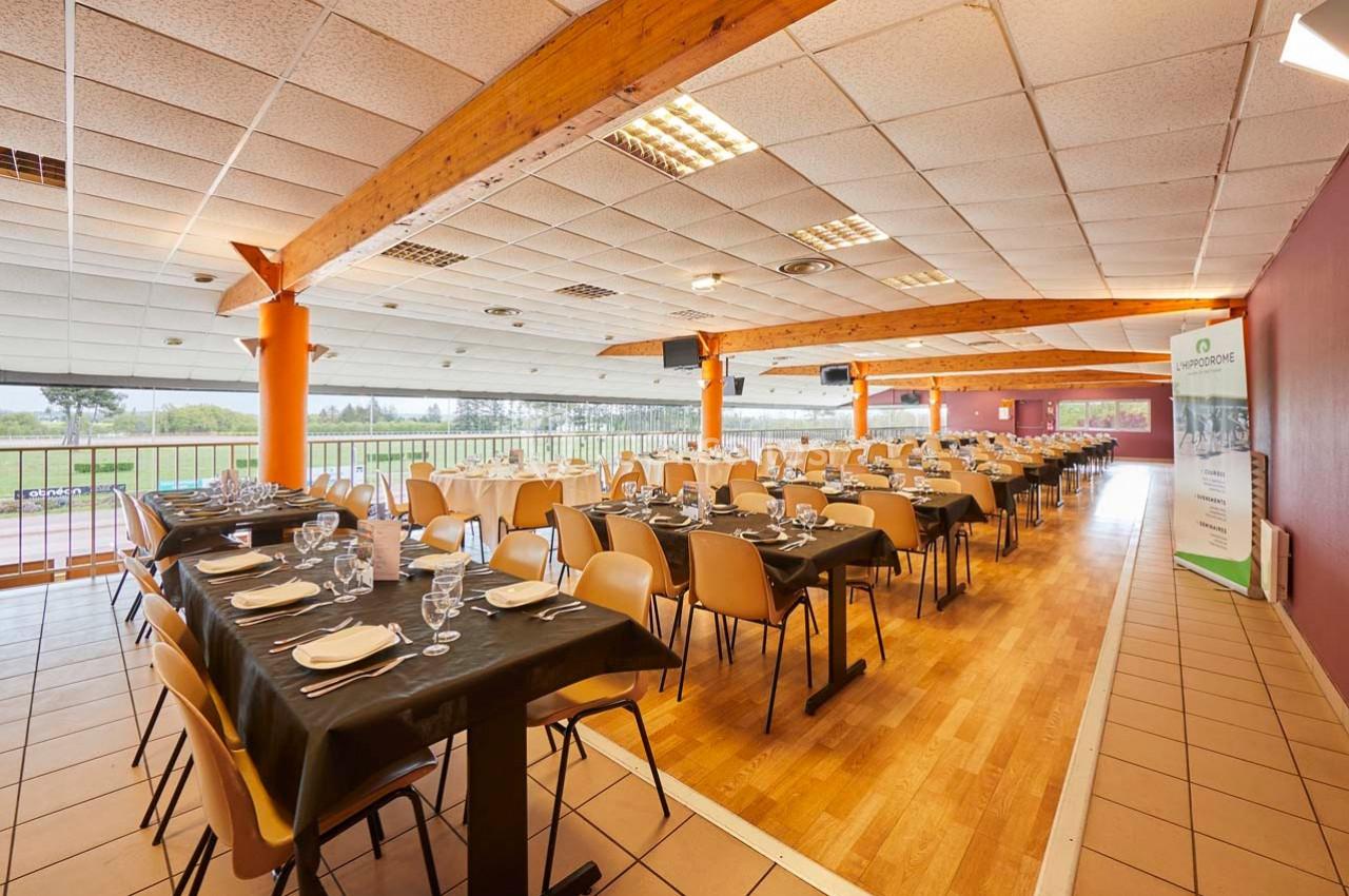 Salle de réception lumineuse avec tables dressées, chaises alignées et vue sur un espace extérieur verdoyant.