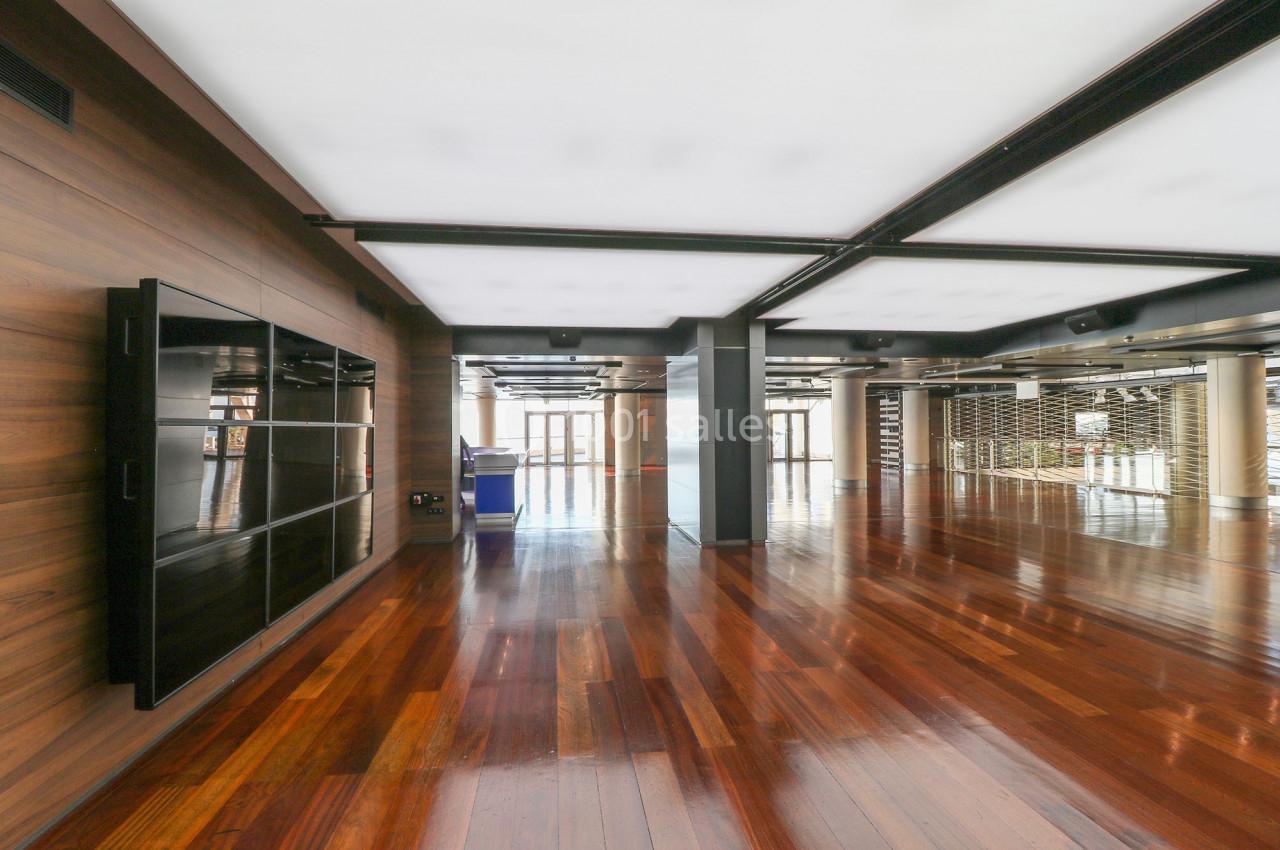 Salle moderne avec parquet en bois brillant, murs en bois, grandes fenêtres et plafond avec éclairage intégré.