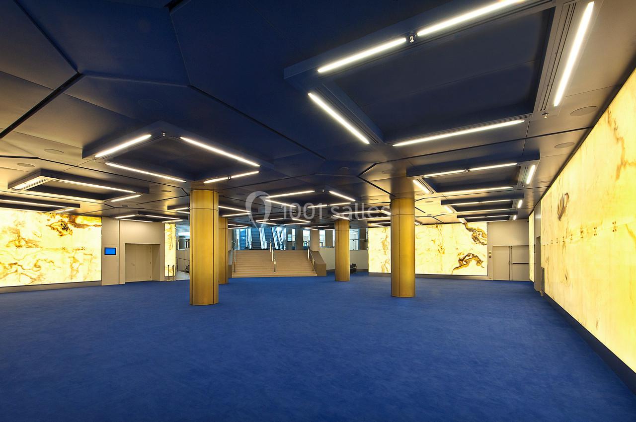 Salle spacieuse avec sol bleu, murs éclairés en jaune doré et plafond moderne avec éclairage intégré.