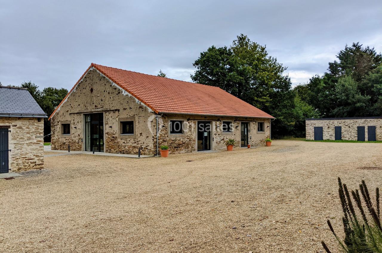 Bâtiment en pierre rénové avec toit en tuiles rouges, entouré d'une cour gravillonnée et de végétation.