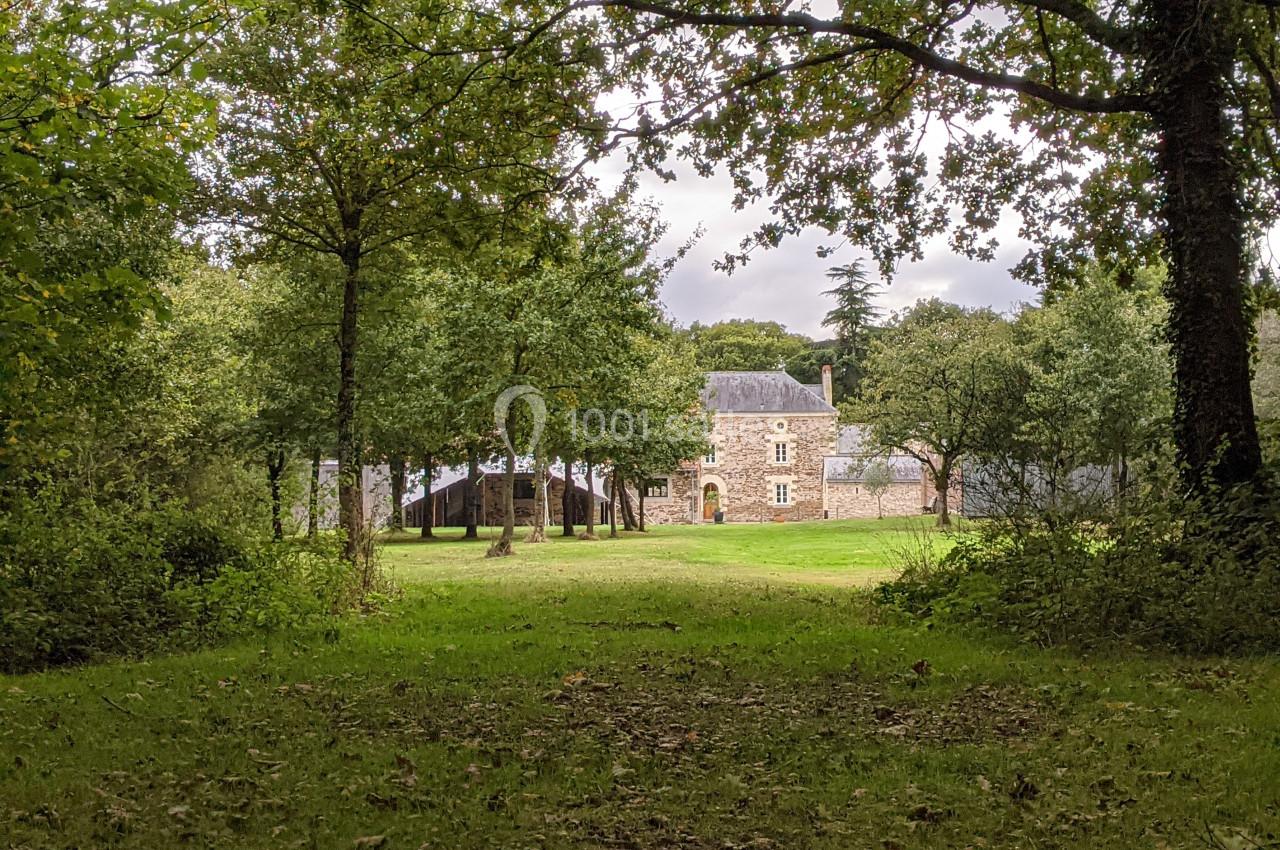 Vue d'une maison en pierre entourée d'arbres et d'une pelouse, dans un cadre naturel verdoyant.