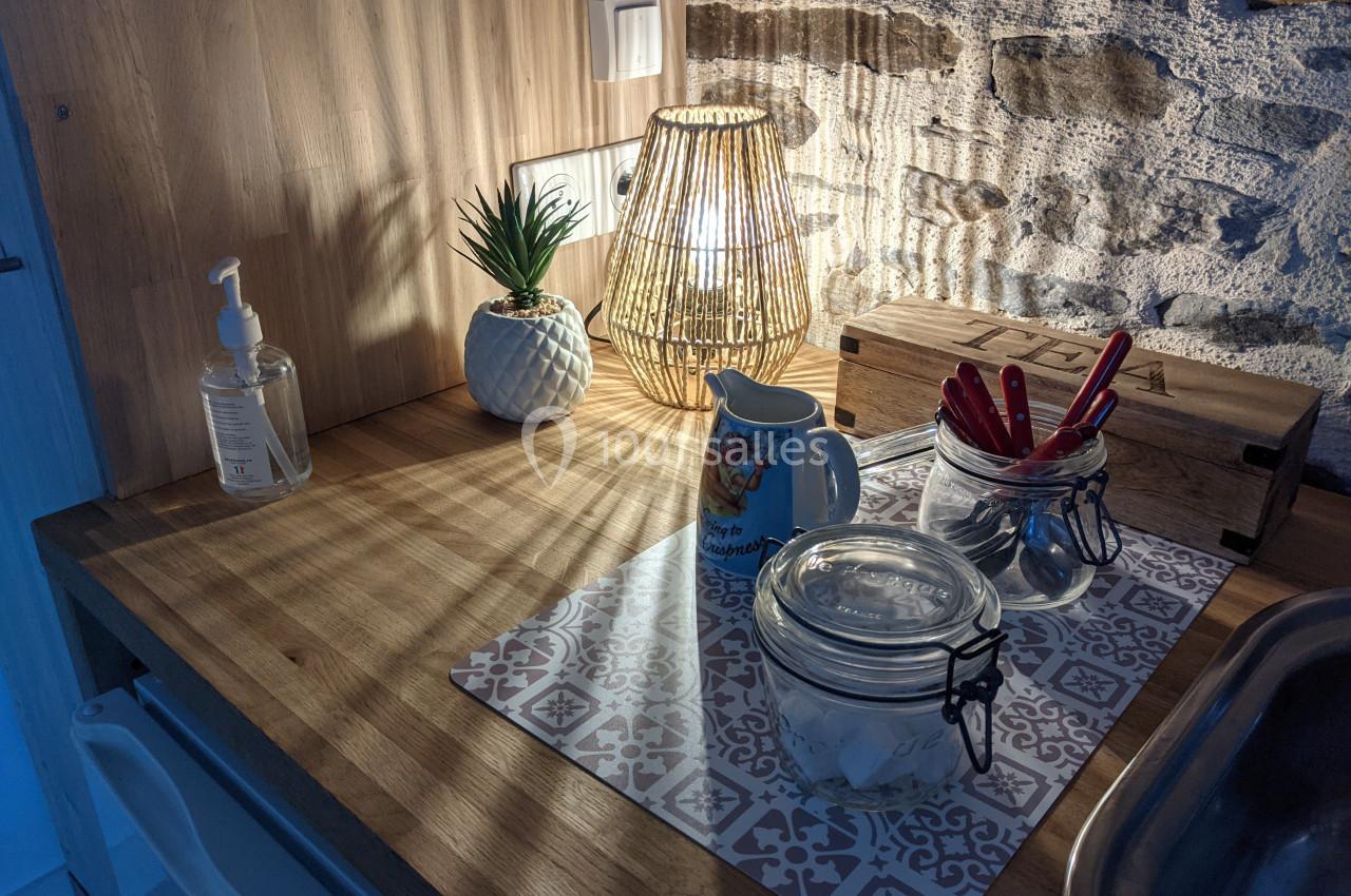 Plan de travail en bois avec lampe allumée, pot de plante, distributeur de savon, bocaux et ustensiles de cuisine.