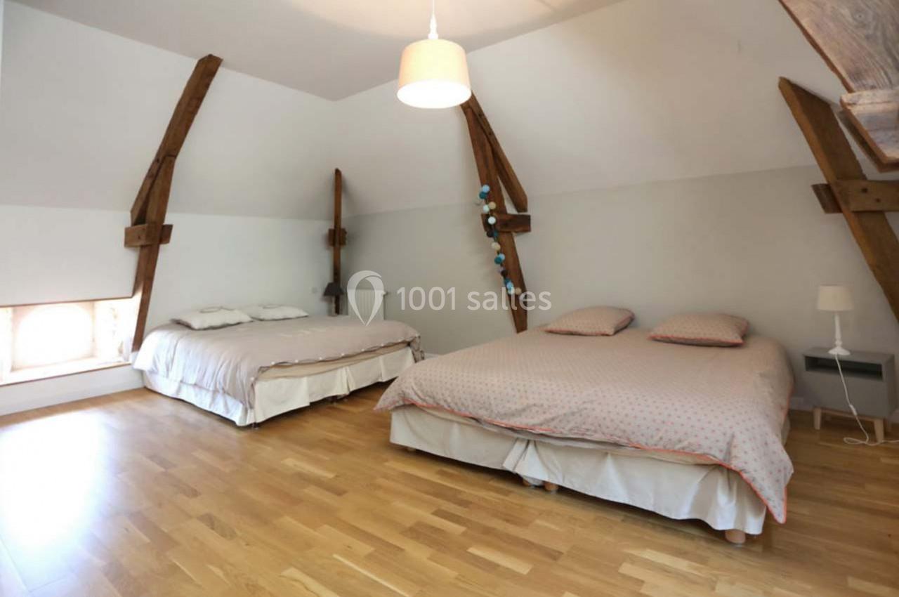Chambre mansardée avec deux lits doubles, parquet en bois clair et poutres apparentes.