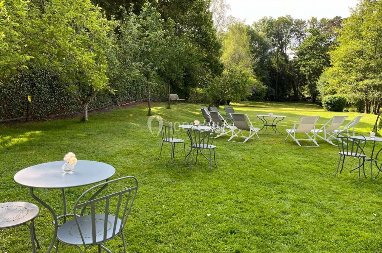 Chaises et tables en métal disposées sur une pelouse verdoyante entourée d'arbres et de haies.