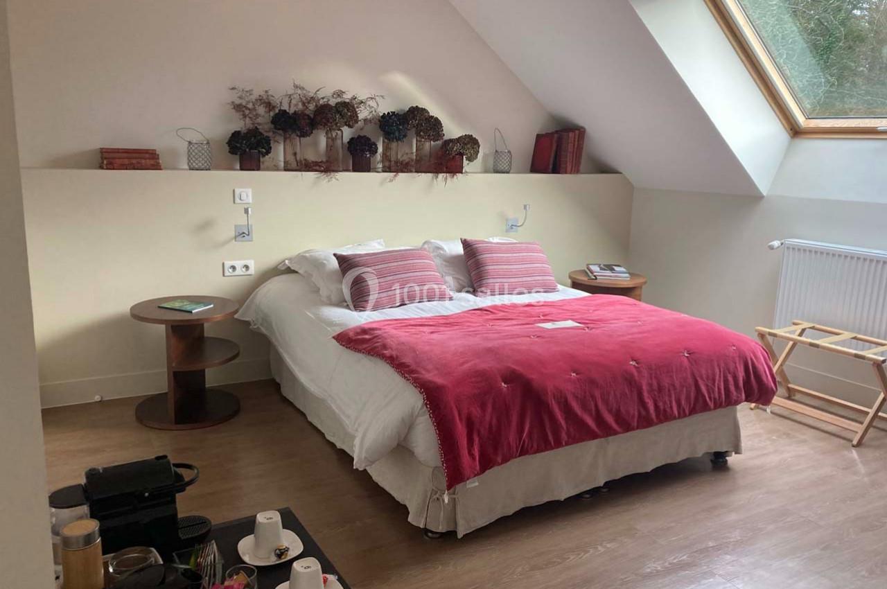 Chambre lumineuse avec lit double, couvre-lit rouge, tables de chevet, fenêtre de toit et plateau d'accueil.