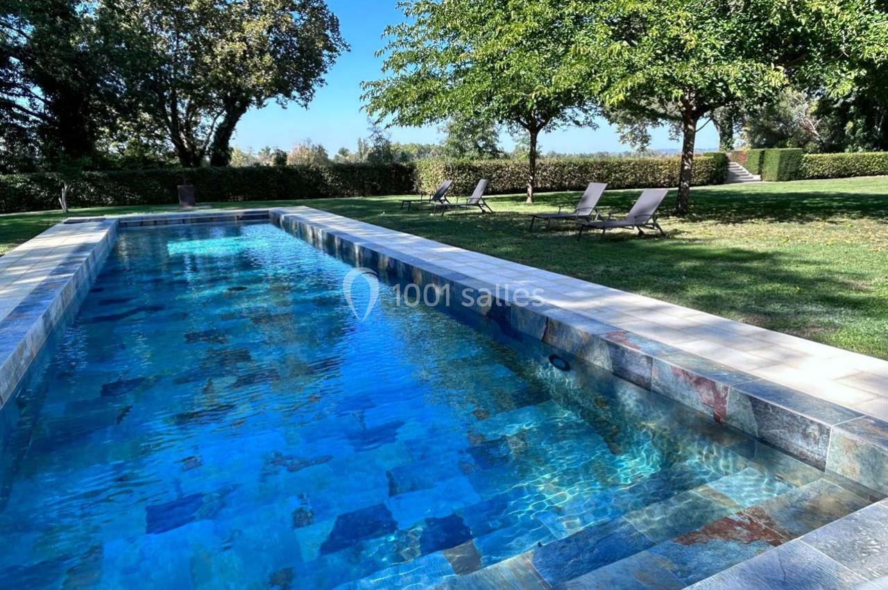 Piscine rectangulaire en pierre entourée de pelouse, avec chaises longues et arbres en arrière-plan.
