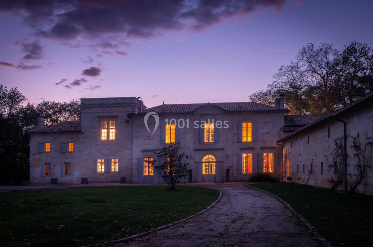 Façade d'un bâtiment en pierre éclairé de nuit, entouré d'arbres et d'un chemin menant à l'entrée.