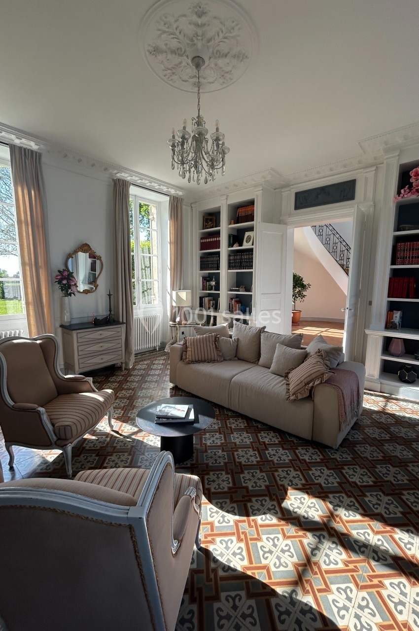 Salon lumineux avec canapé beige, fauteuils assortis, bibliothèque intégrée et carrelage à motifs géométriques.