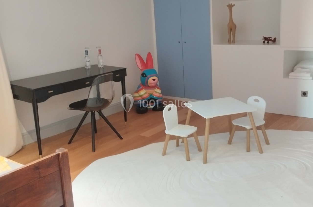 Chambre d'enfant avec bureau, chaise, table et chaises blanches, tapis rond et jouet coloré près d'une armoire bleue.