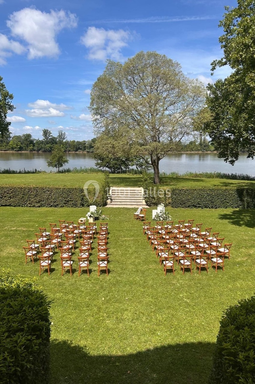 Chaises disposées en rangées sur une pelouse face à un escalier et un arbre, près d'une rivière sous un ciel dégagé.