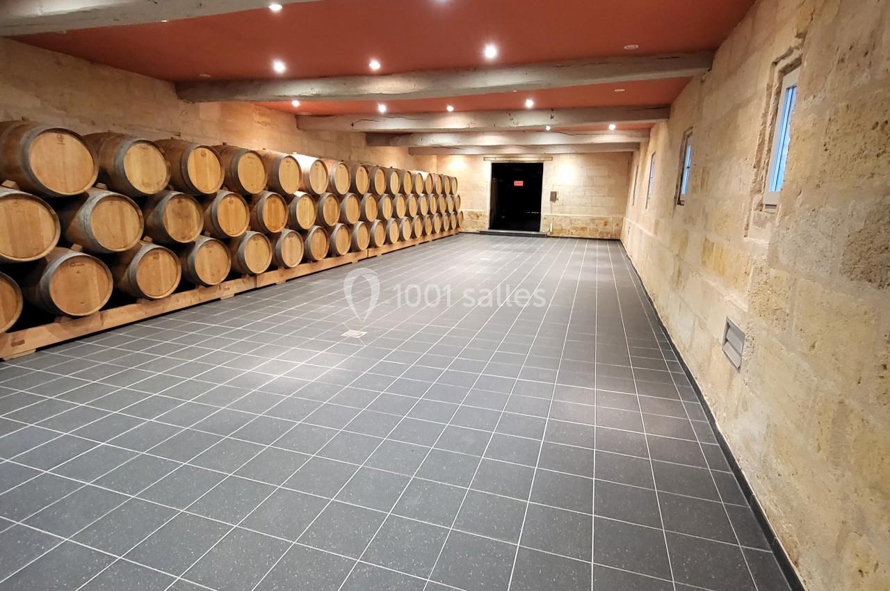 Salle de vieillissement avec des rangées de tonneaux en bois alignés contre un mur en pierre sous un plafond rouge.