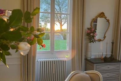 Vue d'un jardin verdoyant avec un arbre central, un escalier en pierre et un lac au coucher du soleil.