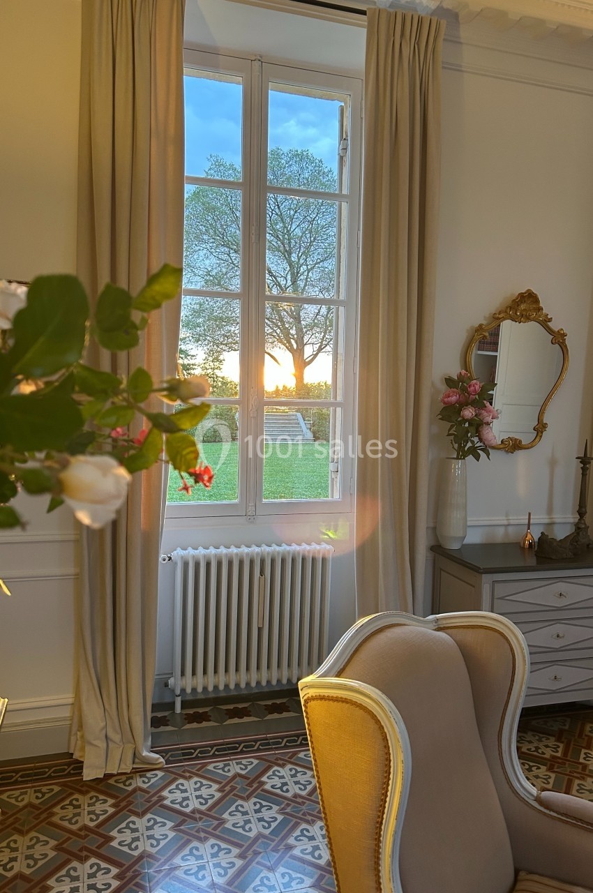 Vue d'une pièce élégante avec fauteuil, fenêtre ouverte sur un coucher de soleil, et détails de décoration classique.