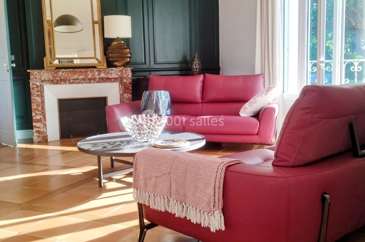 Salon lumineux avec canapé rouge, cheminée en marbre, miroir doré et table basse sur carrelage en terre cuite.