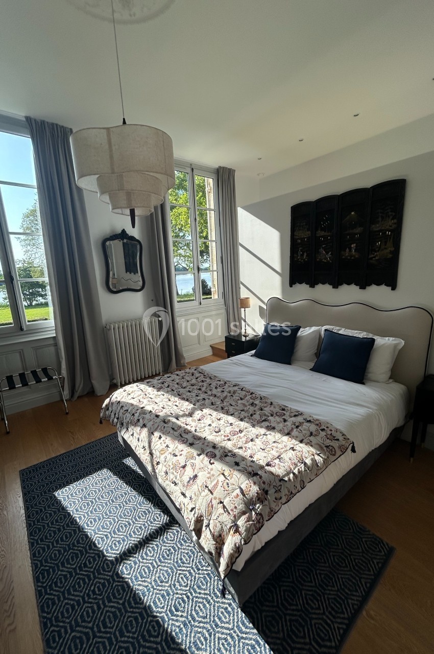 Chambre lumineuse avec un lit double, grande fenêtre donnant sur un paysage verdoyant et décoration élégante.