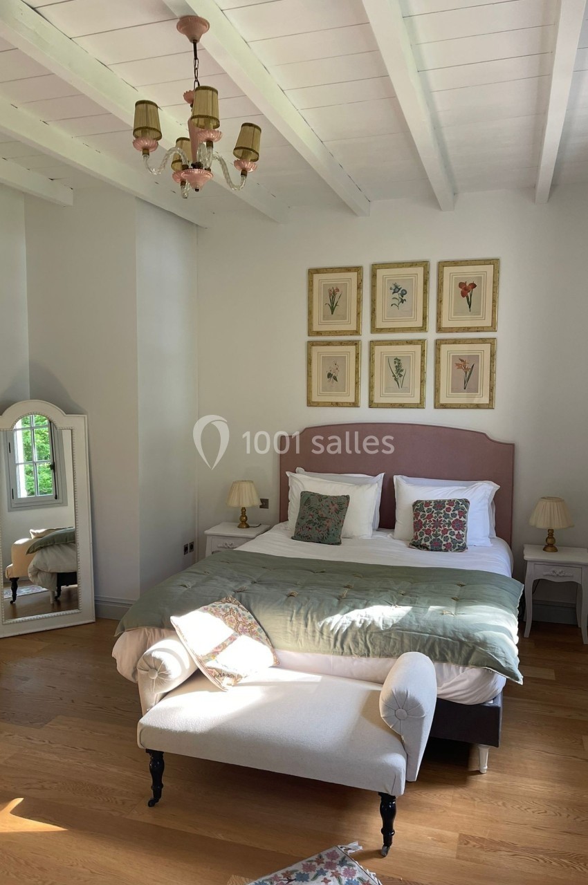 Chambre lumineuse avec lit double, coussins décoratifs, miroir sur pied, plafond à poutres blanches et parquet en bois.