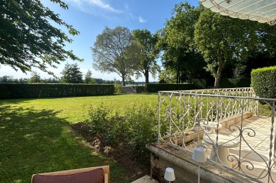 Vue d'un jardin verdoyant avec un arbre central, un escalier en pierre et un lac au coucher du soleil.
