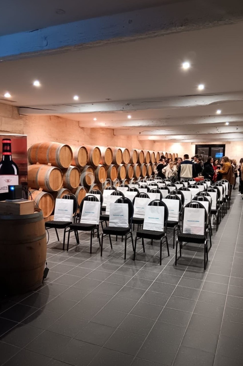 Salle de conférence dans une cave à vin, avec des chaises alignées face à un écran et des tonneaux en arrière-plan.