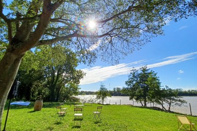 Vue d'un jardin verdoyant avec un arbre central, un escalier en pierre et un lac au coucher du soleil.