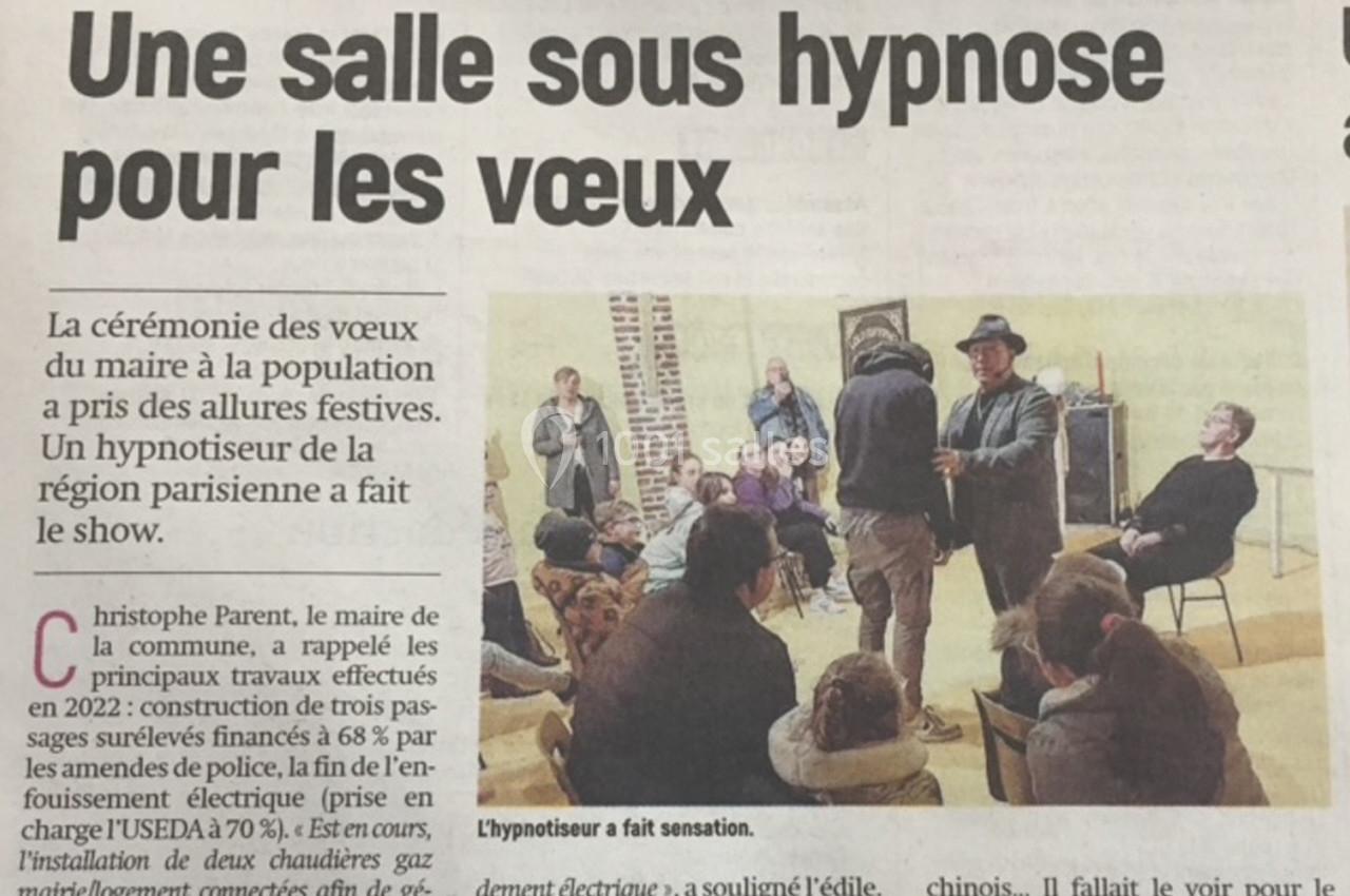 Un hypnotiseur anime une séance devant un public assis dans une salle, lors d'une cérémonie officielle.