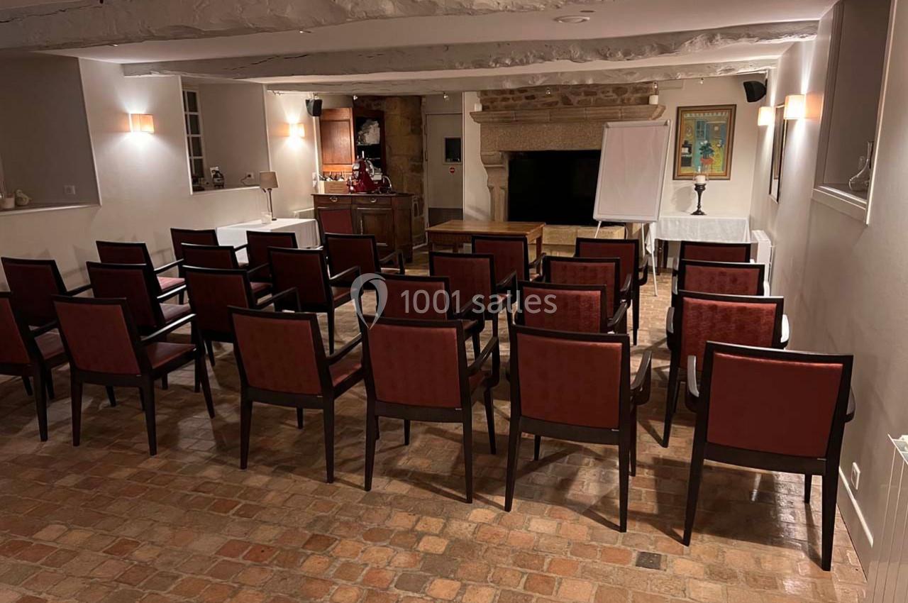 Salle de réunion avec des chaises disposées en rangées face à un tableau blanc et une cheminée en pierre.