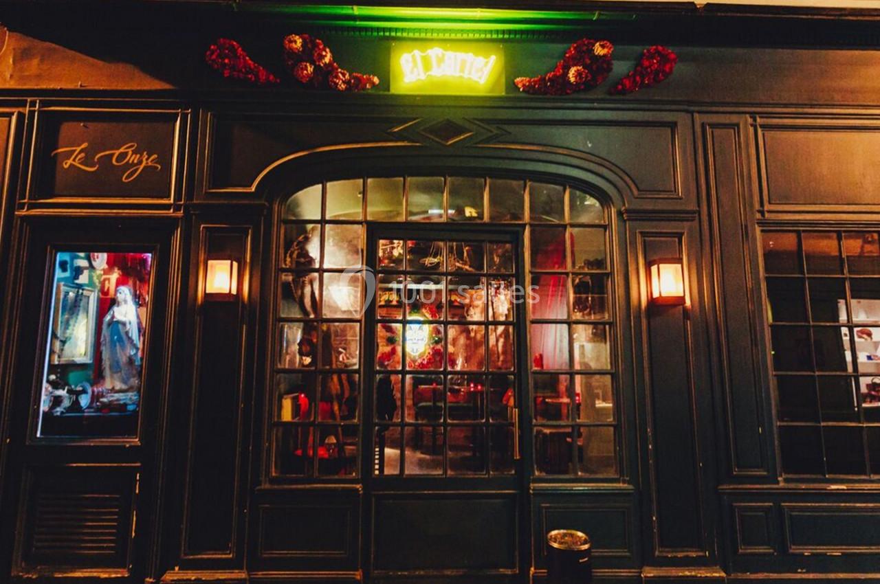 Façade d'une boutique avec une devanture vitrée, éclairée par des lumières chaudes et une enseigne lumineuse verte.