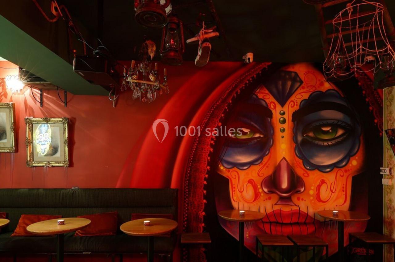 Mur décoré d'une fresque colorée représentant un visage maquillé, entouré de tables et de cadres anciens.