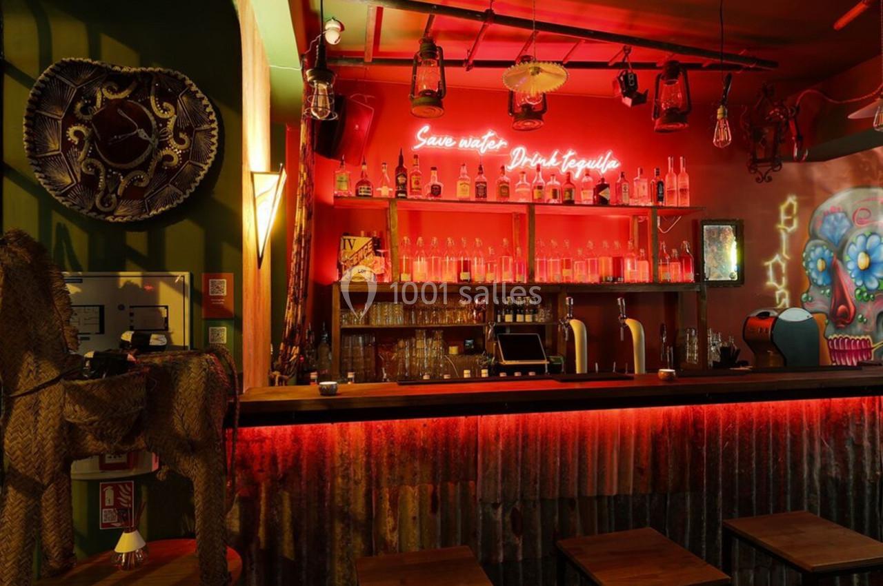 Bar à l'ambiance tamisée avec éclairage rouge, décorations mexicaines et étagères remplies de bouteilles.
