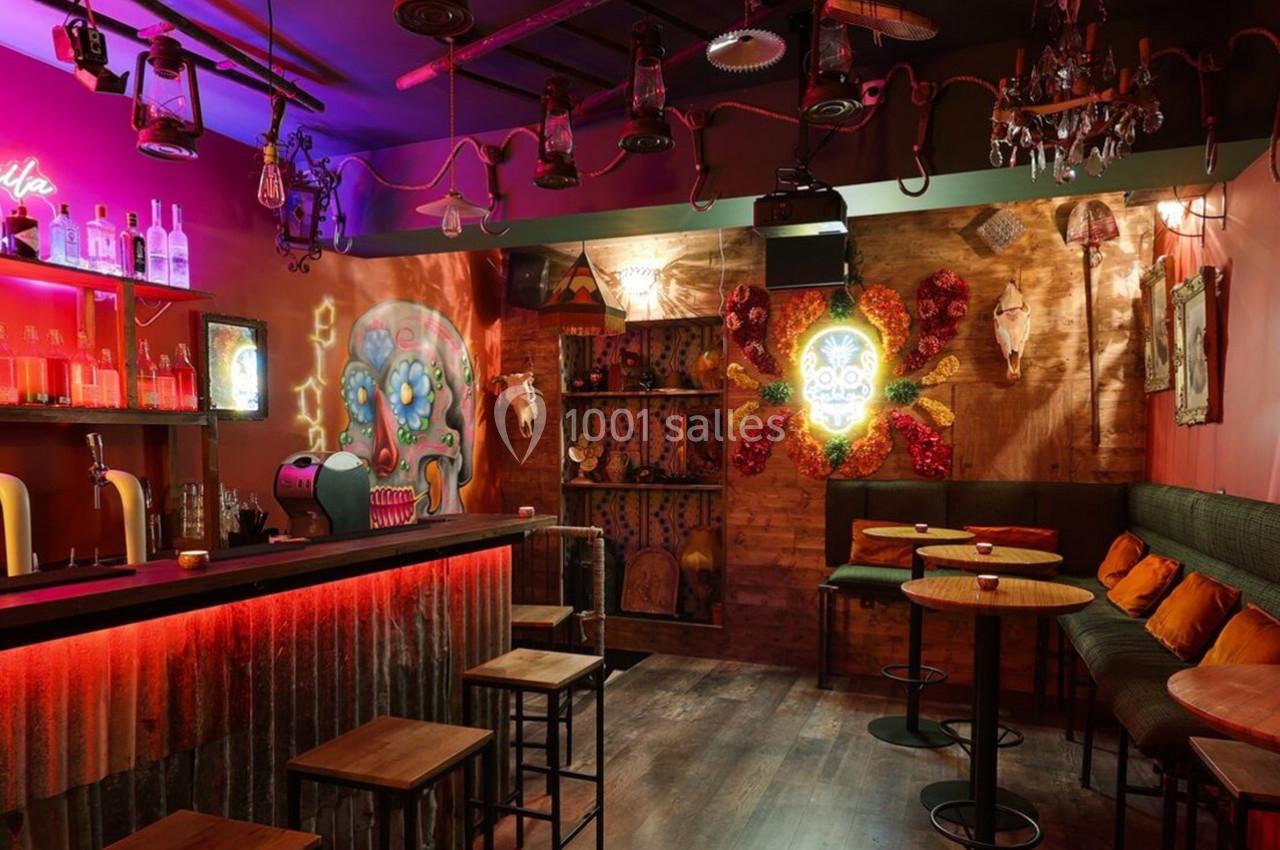 Bar à l'ambiance tamisée avec décorations colorées, tables hautes, banquettes et éclairage rouge.