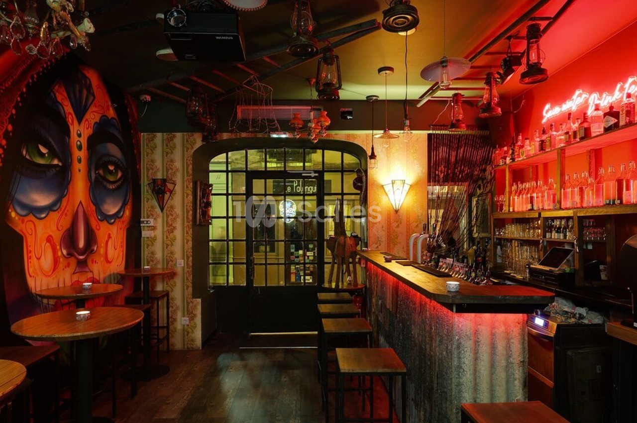 Bar à l'ambiance tamisée avec un mur décoré d'une fresque colorée et un éclairage néon rouge au-dessus du comptoir.