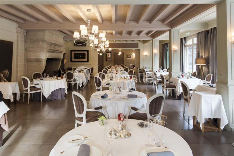 Salle de restaurant élégante avec tables rondes dressées, chaises classiques et éclairage chaleureux.