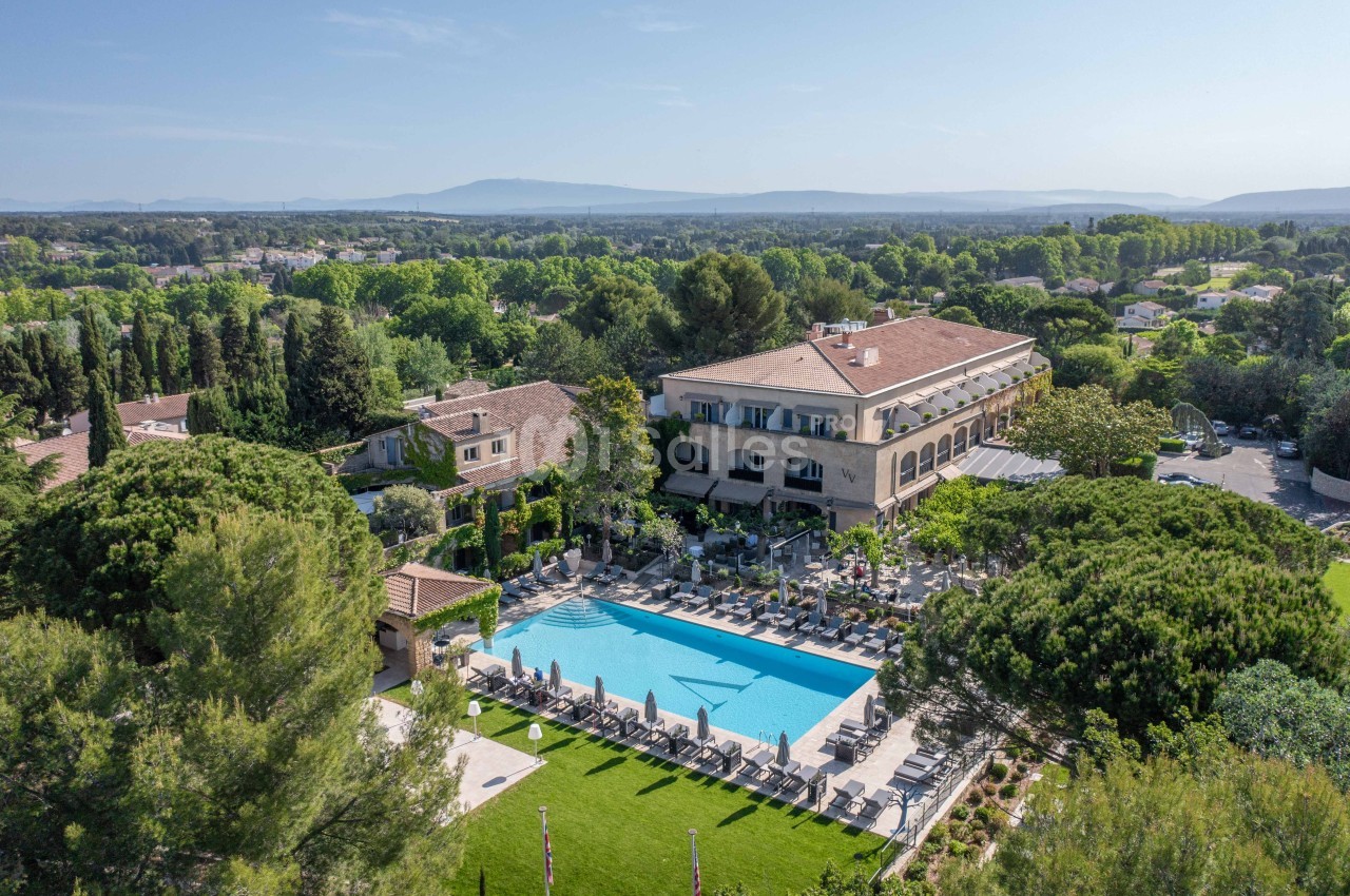 Vue aérienne d'un hôtel entouré de végétation avec une grande piscine et des chaises longues en extérieur.