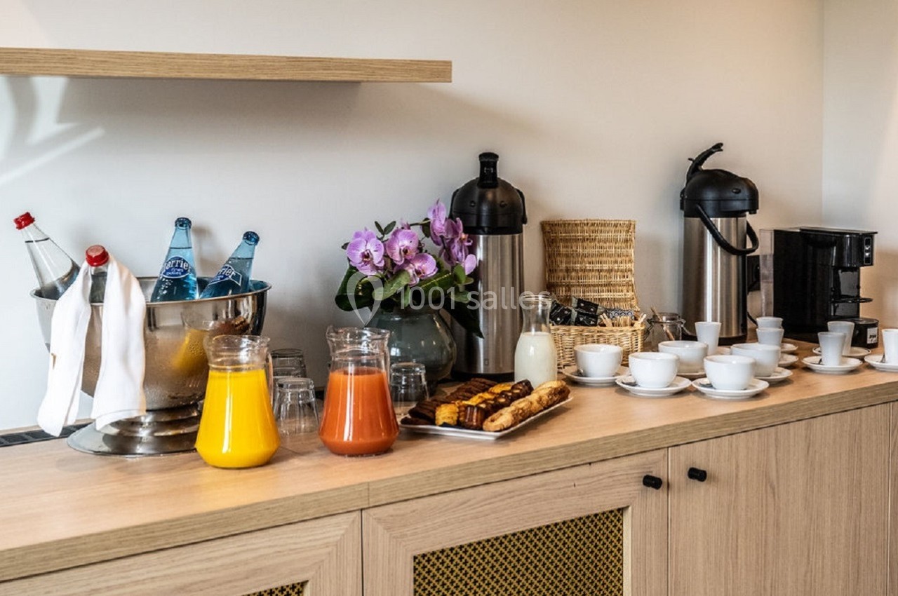 Buffet avec jus, café, thé, viennoiseries, tasses et carafes sur un meuble en bois, décoré d'une orchidée violette.