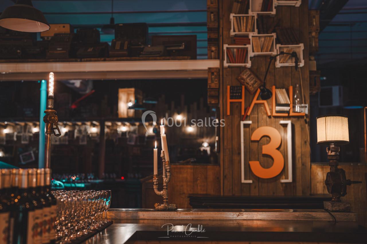 Intérieur d'un bar avec des bougies allumées, des étagères décoratives et un panneau indiquant ’Hall 3’.