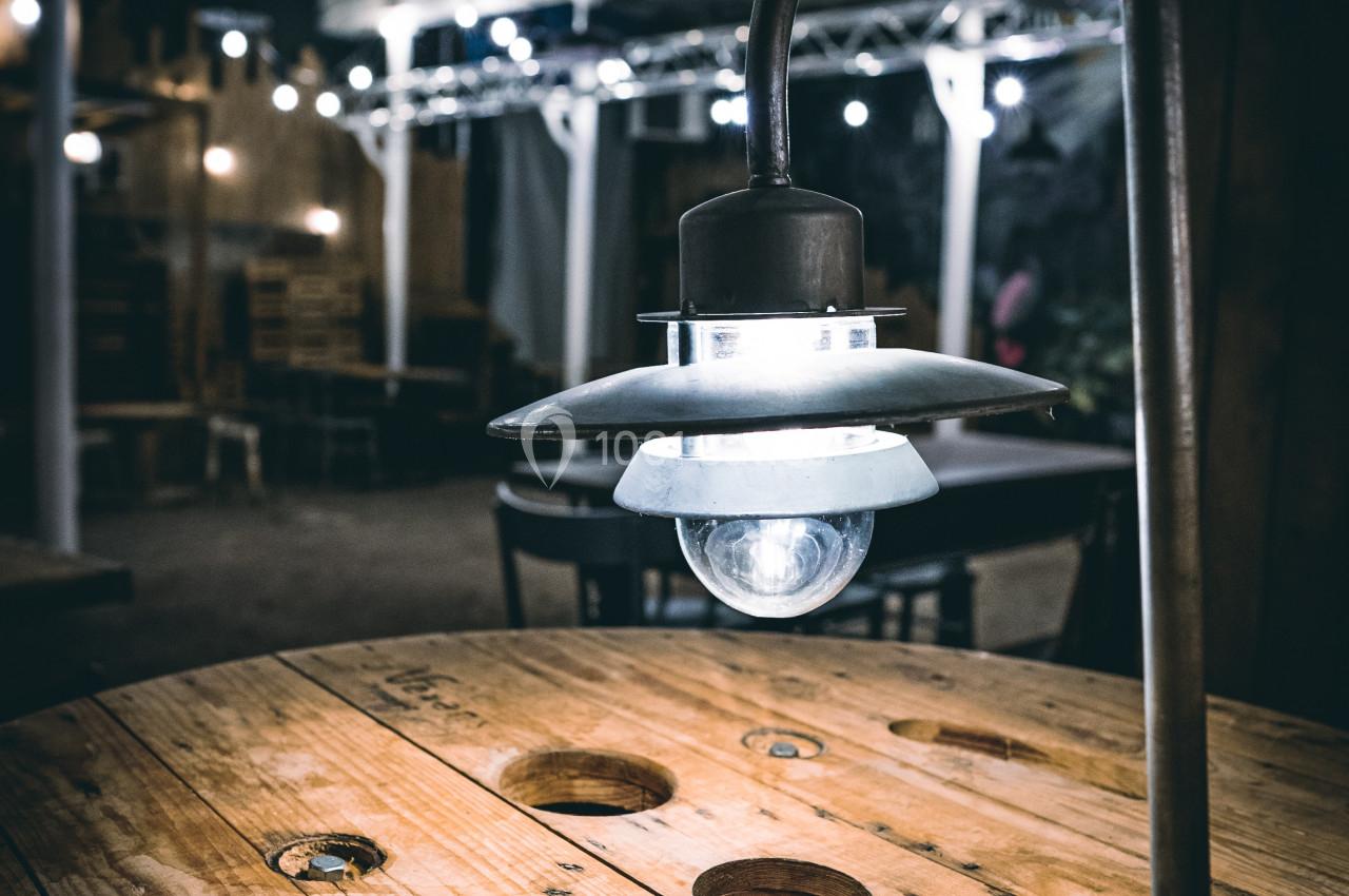 Lampe suspendue au-dessus d'une table en bois dans un espace intérieur faiblement éclairé.